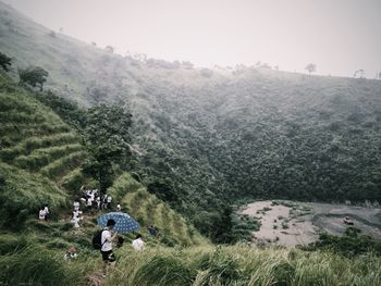 People walking on field by mountains against sky