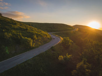 Scenic view of road by mountains against sky during sunset