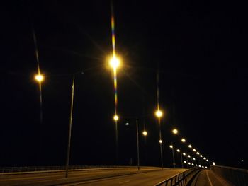 Illuminated street lights on road against sky at night