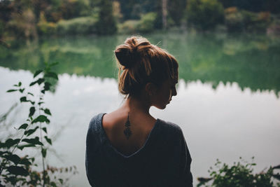 Woman standing by lake against trees