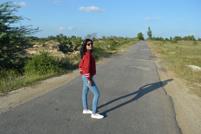 Full length portrait of young woman standing on road against sky