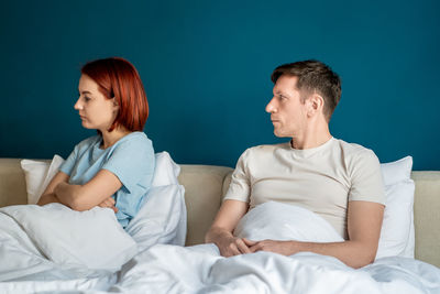 Side view of couple sitting on bed at home