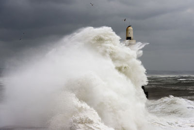 Sea waves splashing on shore against sky