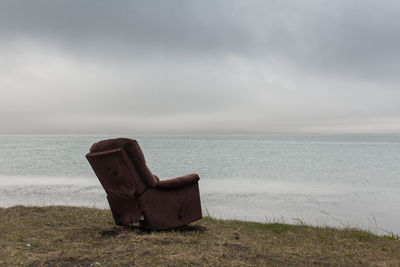 Abandoned chair on beach against sky