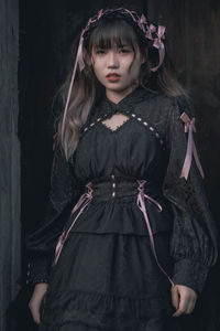 Portrait of young woman standing against black background