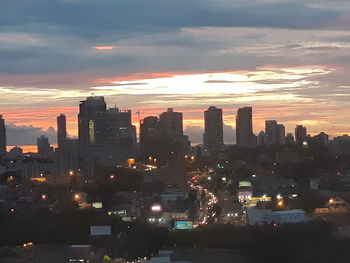 Illuminated buildings in city against sky during sunset