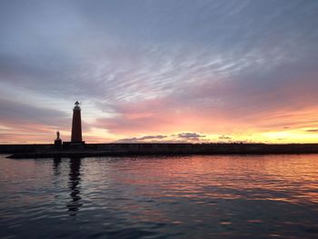 Silhouette lighthouse by sea against sky during sunset