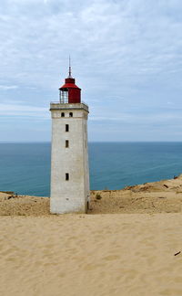 Lighthouse on beach by sea against sky