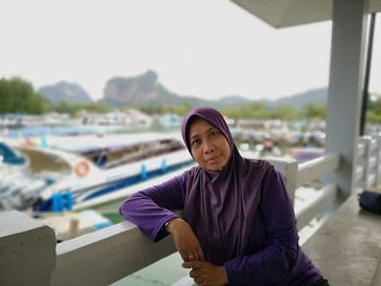 Portrait of woman wearing hijab sitting at harbor