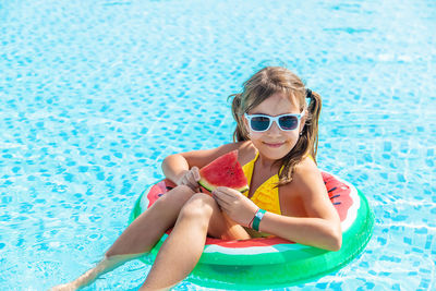 Portrait of smiling girl eating watermelon in swimming pool