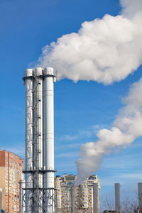 Puffs of smoke and steam rise into the sky from an urban thermal plant in a residential city block.