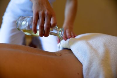Midsection of woman pouring essential oil on customer back at spa