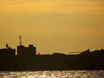 Silhouette buildings by sea against sky during sunset