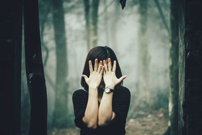 Woman covering face with hands while standing against trees