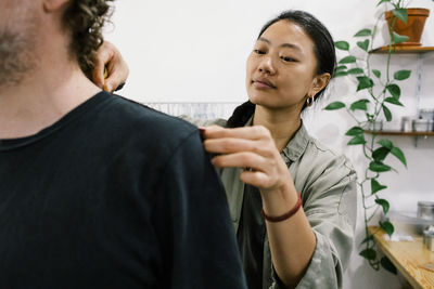 Female tailor measuring shoulder of male customer at workshop