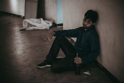 Young woman sitting on floor against wall at home