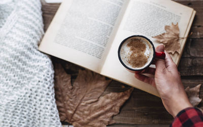 Female hand holding cup of coffee while reading a book in autumn