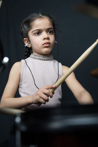 Girl wearing hearing aid while playing drum against wall