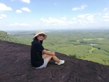 Young woman sitting on landscape against sky