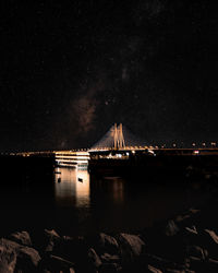 Illuminated bridge over river against sky at night