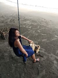 Young woman sitting on beach by sea against sky