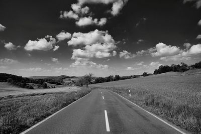 Empty road amidst field against sky