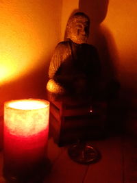 Close-up of illuminated statue on table against wall