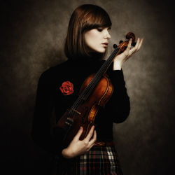 Young woman holding violin while standing against wall