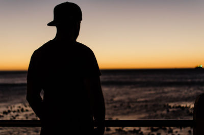 Silhouette man looking at sea against sky during sunset
