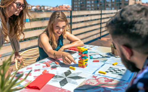 Woman looking jenga game piece next to colleagues on terrace