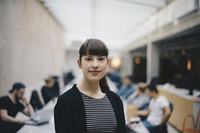 Portrait of female confident computer programmer at office with colleagues working in background
