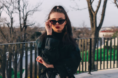 Portrait of young woman standing by railing