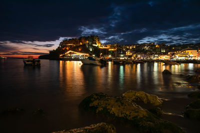 Illuminated greek town by sea against sky at night