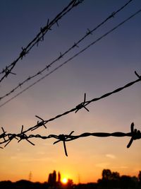 Silhouette of barbed wire against sky during sunset