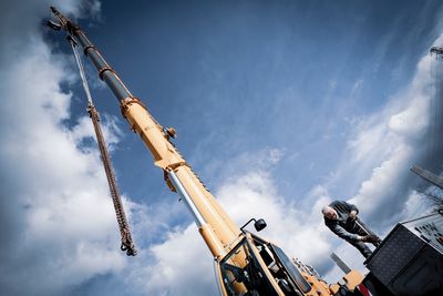 Low angle view of cranes at construction site against sky