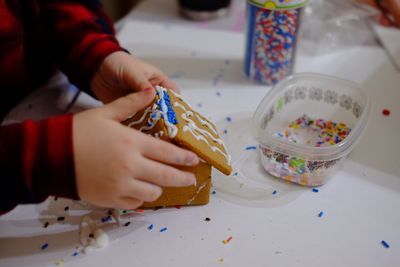 Cropped hand making gingerbread house on table