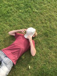 High angle view of boy sleeping on grassy field while face covered with cap