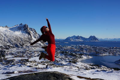 Full length of woman jumping on snow covered mountain