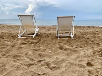 Deck chairs on beach against sky