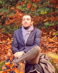 Portrait of young man sitting on sidewalk during autumn