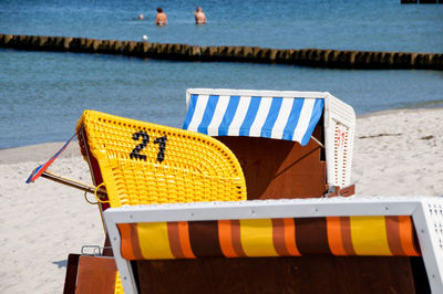 Close-up of hooded chairs with people swimming in background at beach