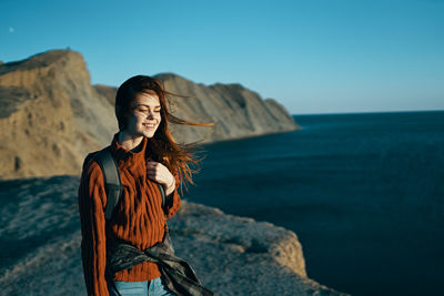 Woman standing on rock by sea against sky