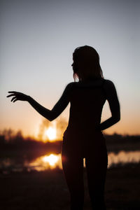 Rear view of silhouette woman standing against sky during sunset