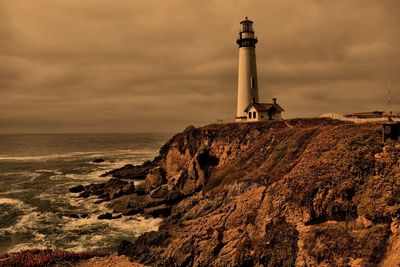 Lighthouse on beach against cloudy sky