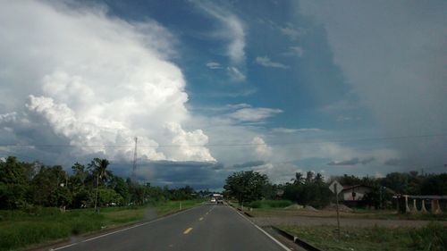 Road passing through field against cloudy sky