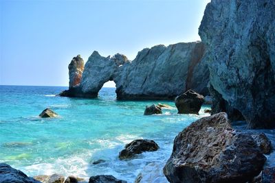 Rocks in sea against clear blue sky