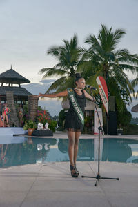 Woman standing by swimming pool against palm trees