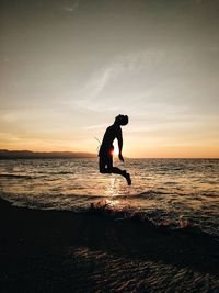 Silhouette man jumping in sea against sky during sunset