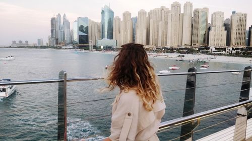 Rear view of woman looking at modern buildings while standing by railing in city