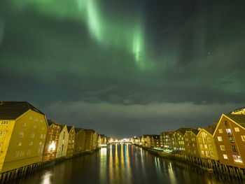 Canal in illuminated city against aurora borealis